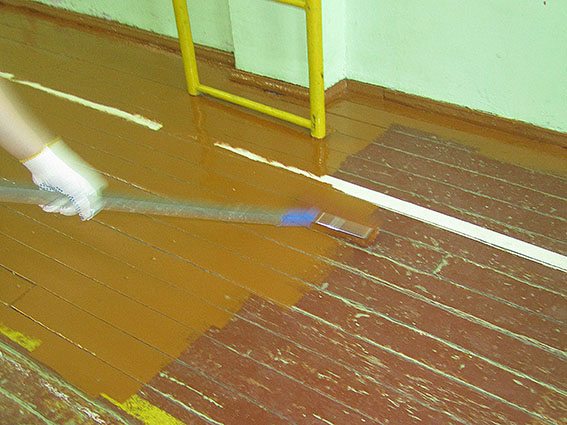 На фото - процесс окрашивания старого деревянного пола в спортзале